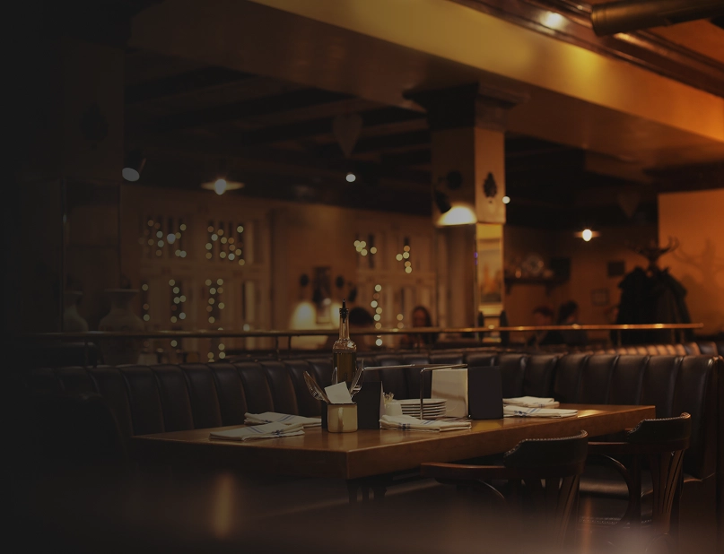 Przytulne wnętrze restauracji z drewnianym stołem, skórzanymi kanapami i ciepłym oświetleniem.