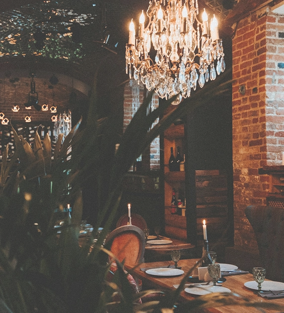 Elegancka, nastrojowa restauracja z ceglanymi ścianami, świecami, drewnianymi stołami i efektownym kryształowym żyrandolem.