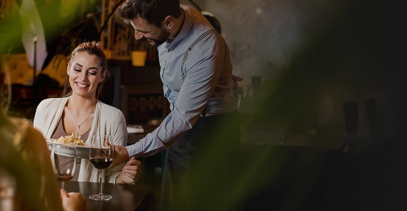 Kelner podający danie kobiecie przy stoliku w przytulnej restauracji z ciepłym oświetleniem.